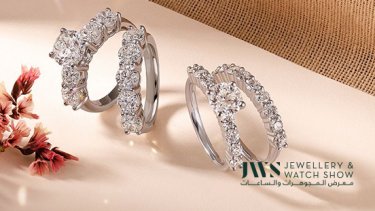 A pair of diamond solitaire and twin band rings placed beside some flowers 