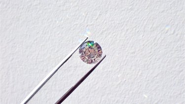 Diamond held between tweezers on a white wall