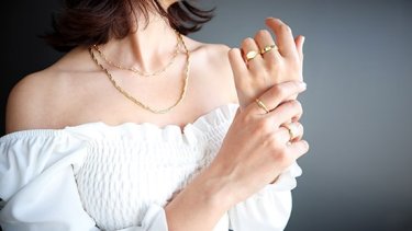 Woman posing to show off gold rings and gold necklace